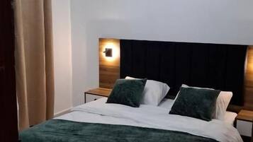 Un dormitorio con cama, mesitas de noche, cabecera y lámpara de techo.