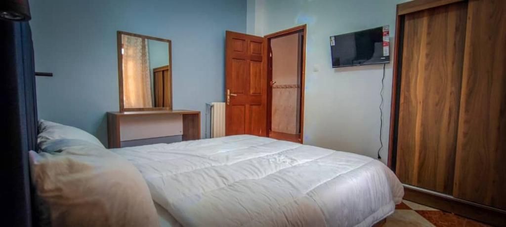 Un dormitorio con una cama, un armario de madera, un espejo y un televisor en la pared.