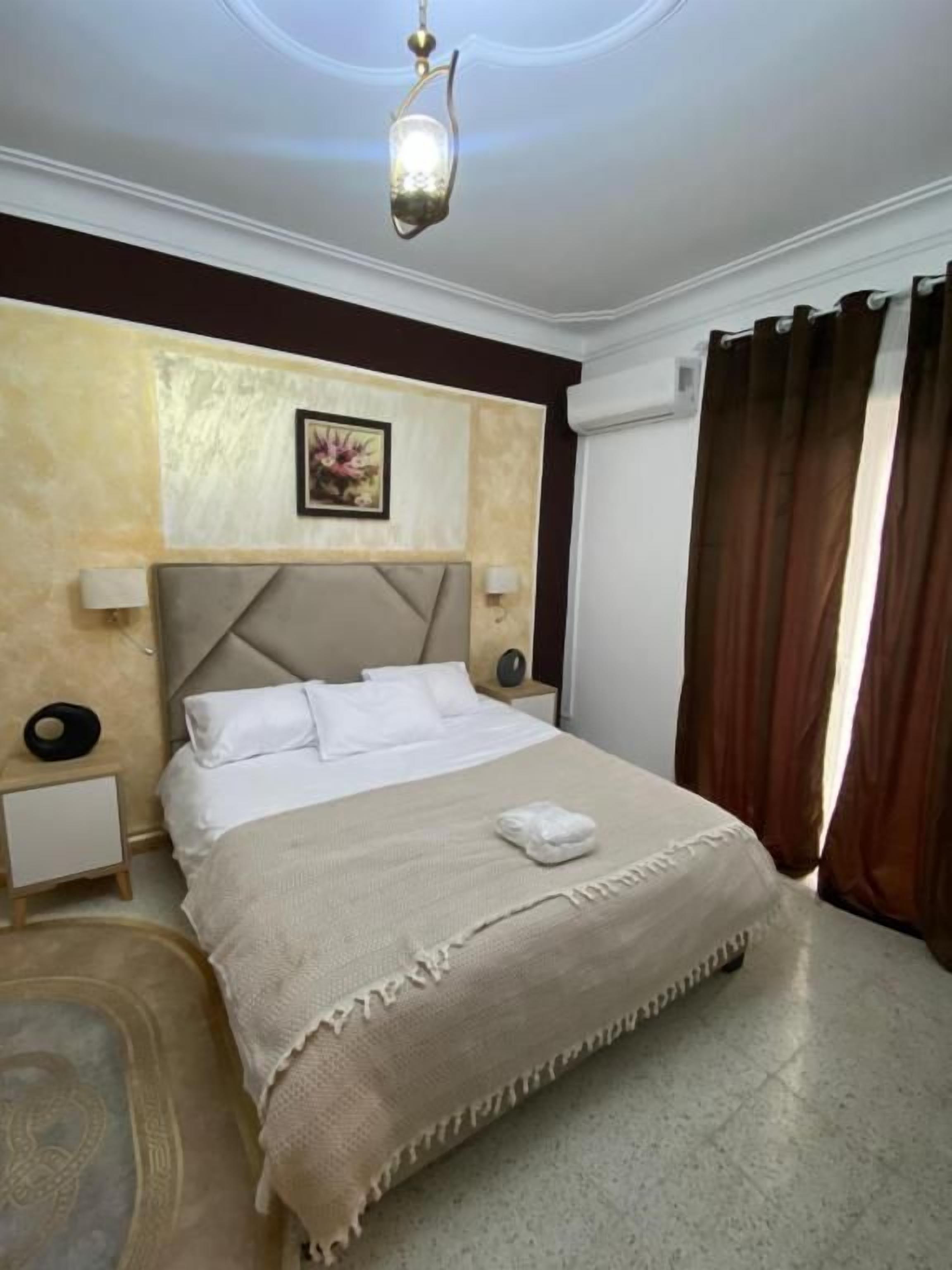 Una habitación de hotel con una cama grande, cabecera, lámparas de noche, alfombra y lámpara de techo.