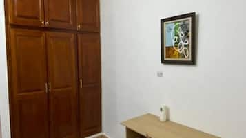 A room with a wooden wardrobe, a desk with a chair, and a framed picture on the wall.