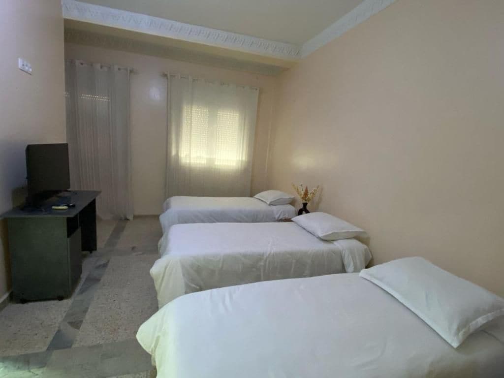 Habitación de hotel con tres camas, un escritorio y una televisión.