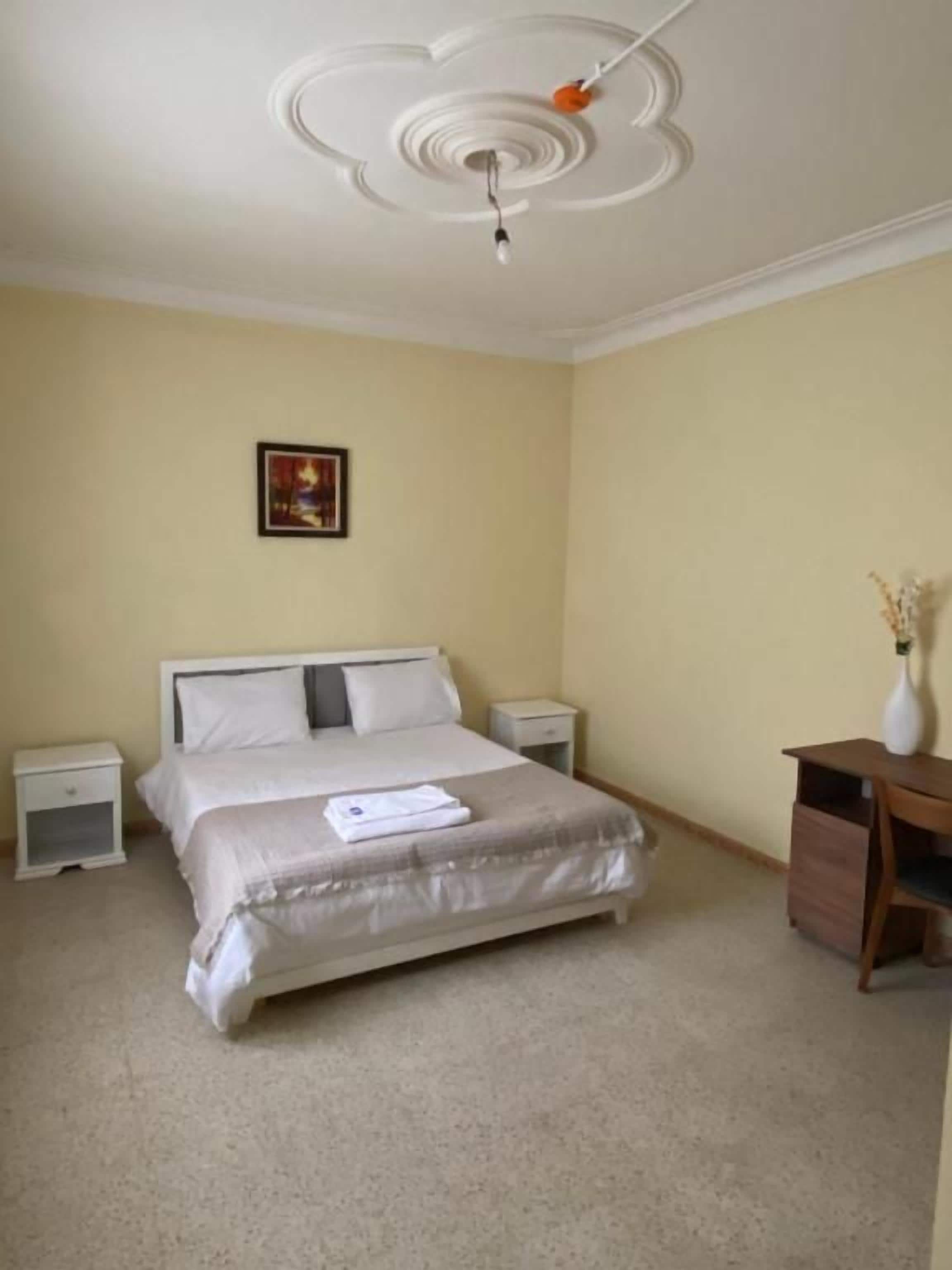 Un dormitorio con cama, mesitas de noche, escritorio y ventilador de techo.