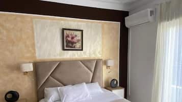 Habitación de hotel con una cama grande, cabecera, dos mesitas de noche, aire acondicionado de pared y una ventana con cortinas.