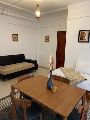 Habitació amb taula de dinar de fusta, dues cadires, un sofà, un llit i un vas amb flors.