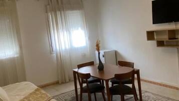 Habitación de hotel con cama, mesa de comedor con sillas, un televisor pequeño en la pared y una alfombra estampada.