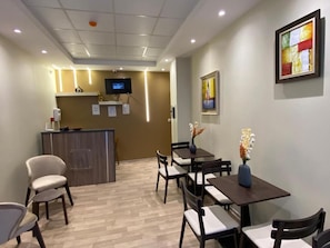 A reception area with a counter, chairs, tables, and a television. - Hostel apart family (dar el beida)