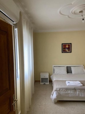 Un dormitori amb un llit, una tauleta de nit, una porta i un ventilador de sostre.