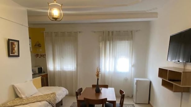 Habitación compacta con cama, una mesa de comedor con sillas, un televisor pequeño y un tapete decorativo.