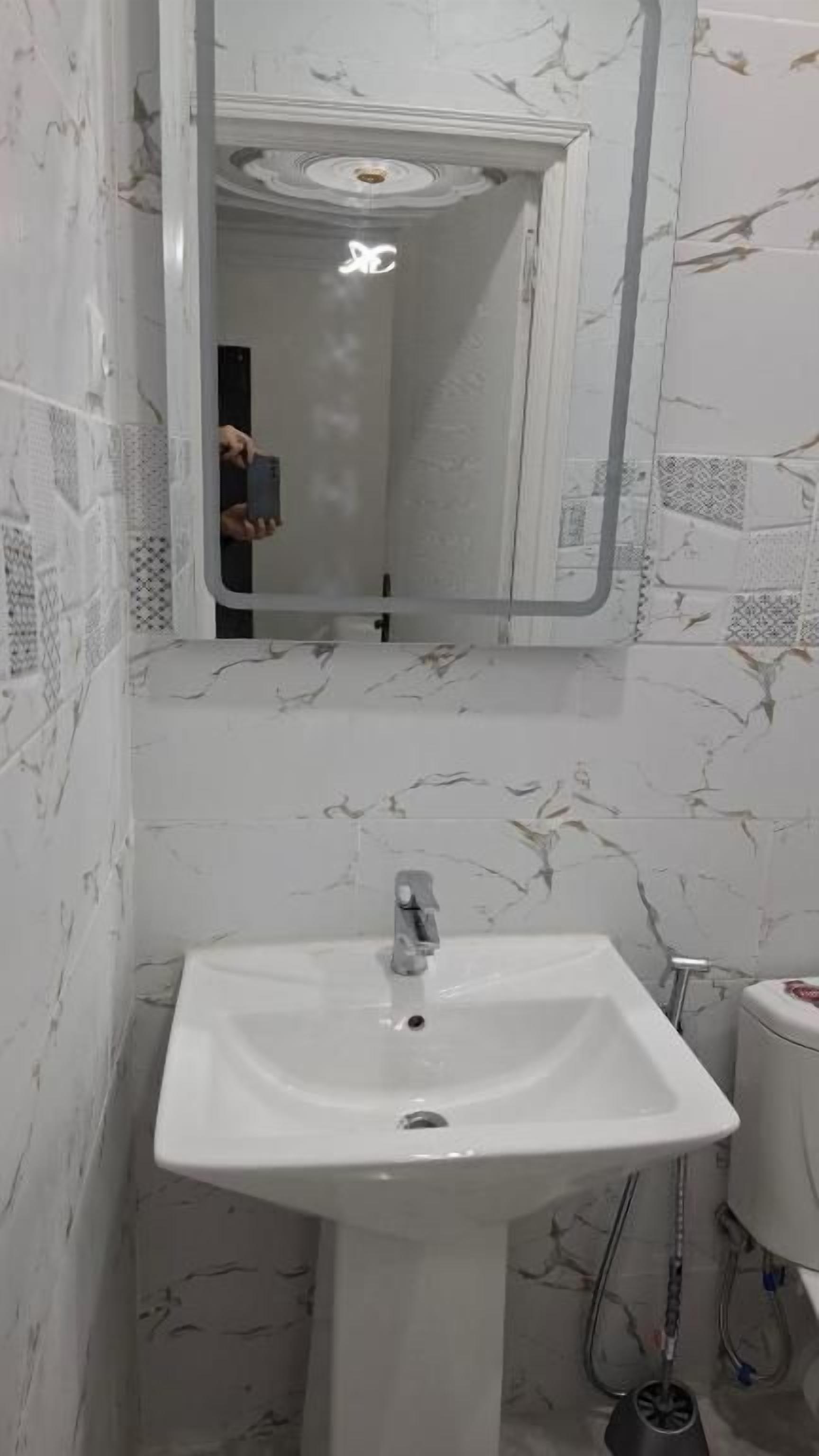 Un baño con lavamanos blanco, un espejo y baldosas estampadas en las paredes.