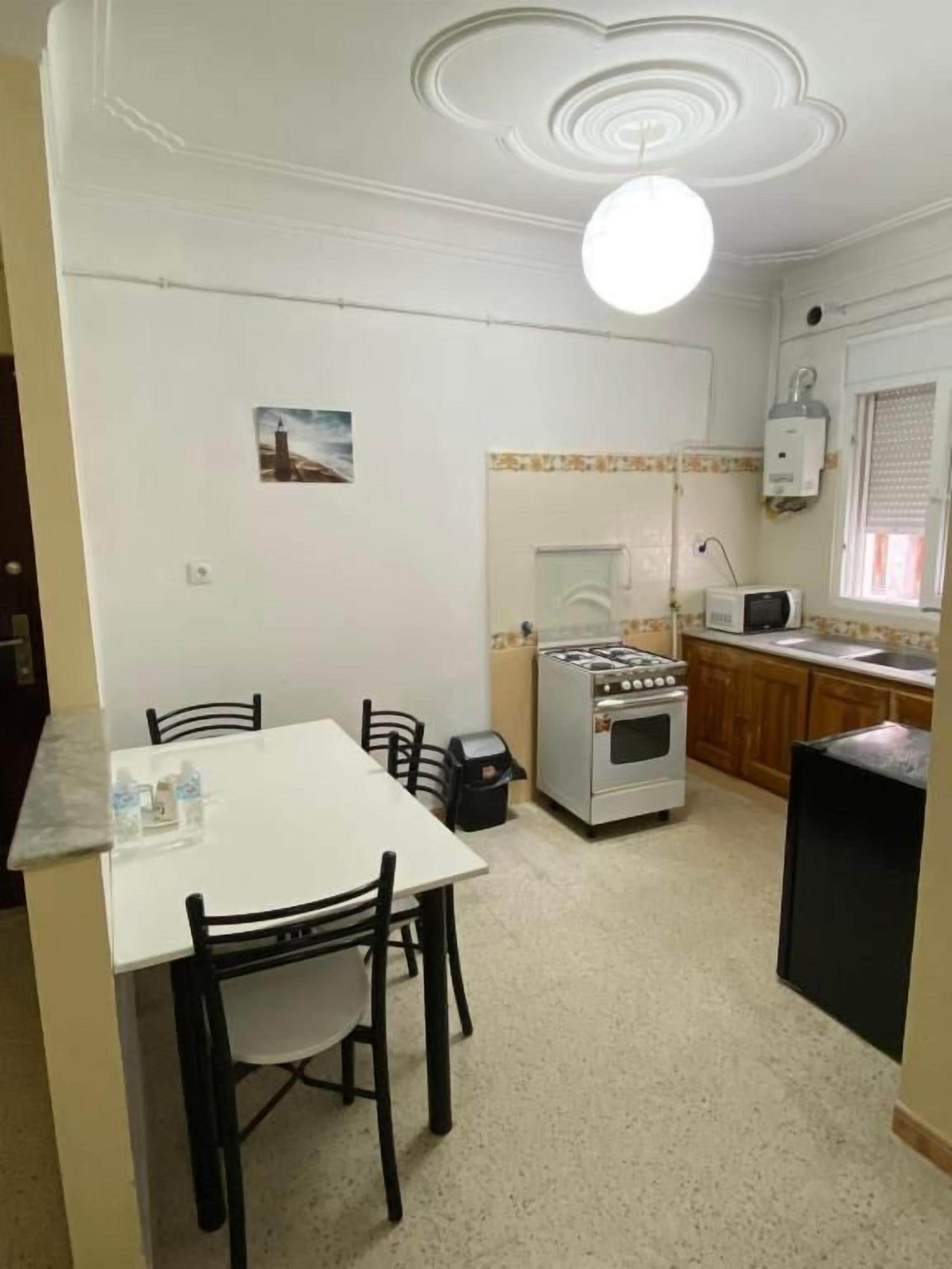 Una cocina compacta con una mesa y sillas blancas, estufa y microondas.