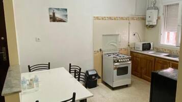 Una cocina compacta con una mesa y sillas blancas, estufa y microondas.