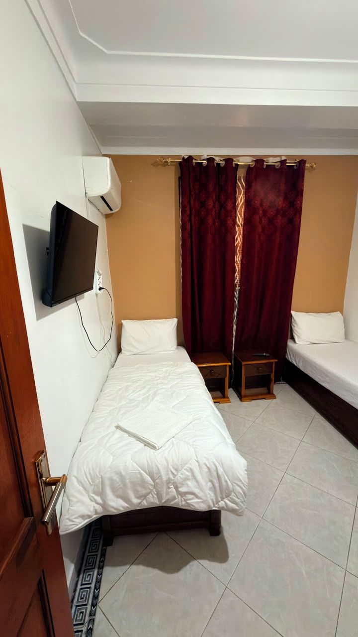 Una habitación con una cama, un televisor montado en la pared y una ventana con cortinas.