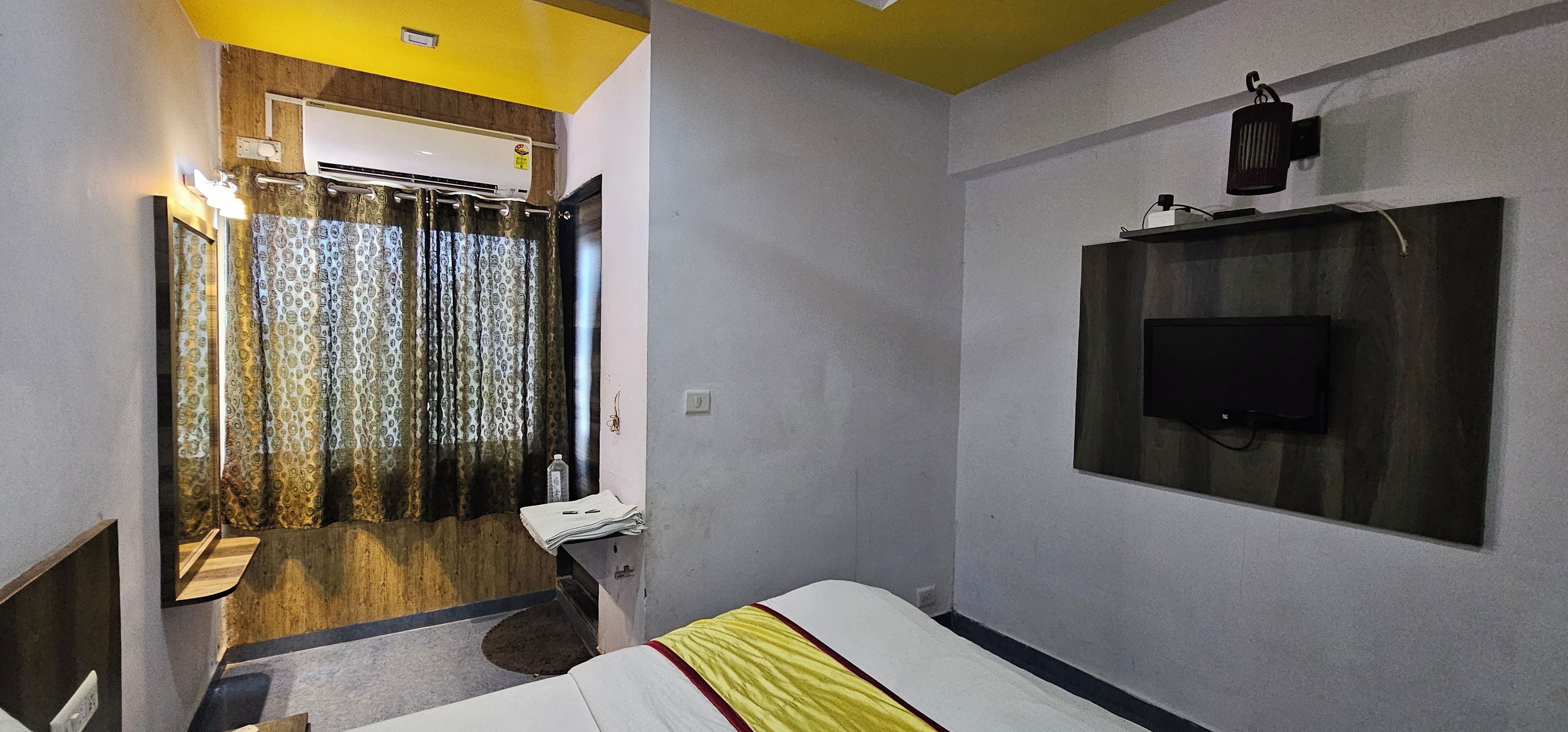 A hotel room with a bed, a television mounted on the wall, a bathroom with a shower, and a curtain.