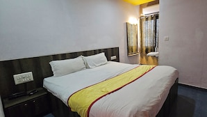 A hotel room with a bed, a nightstand, a mirror, and a window with curtains. - Hotel Signature (Ahmedabad)