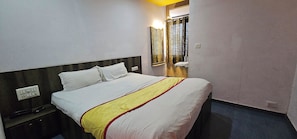 A hotel room with a bed, a nightstand, a mirror, and a window with curtains. - Hotel Signature (Ahmedabad)