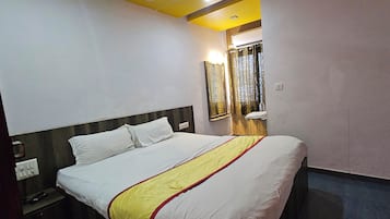 Een hotelkamer met een bed, een nachtkastje, een spiegel en een raam met gordijnen.