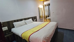 A hotel room with a bed, a nightstand, a mirror, and a window with curtains. - Hotel Signature (Ahmedabad)