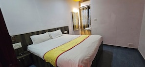 A hotel room with a bed, a nightstand, a mirror, and a window with curtains. - Hotel Signature (Ahmedabad)