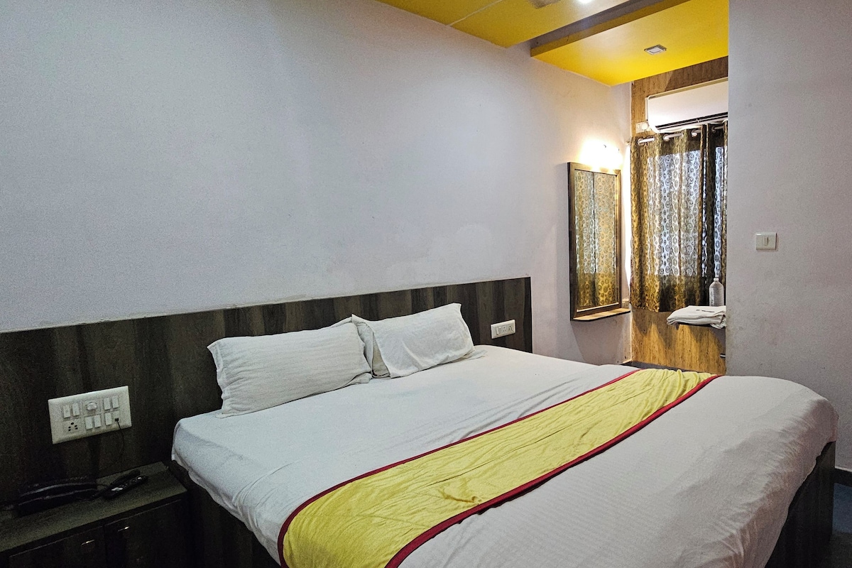 A hotel room with a bed, bedside table, and a mirror.