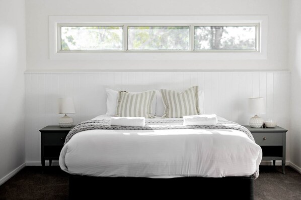 A bedroom with a bed, two bedside tables, a window, and a nightstand.