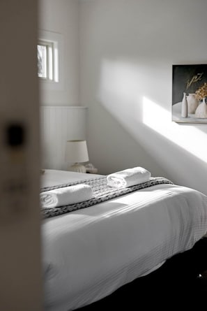 Ein Schlafzimmer mit einem Bett, einer Nachttischlampe, einem Fenster und einem Bild an der Wand.