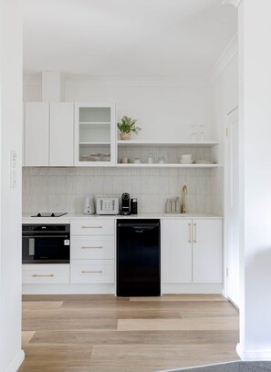 Una cocina moderna con muebles blancos, lavavajillas negro y una encimera con cafetera y tostadora.