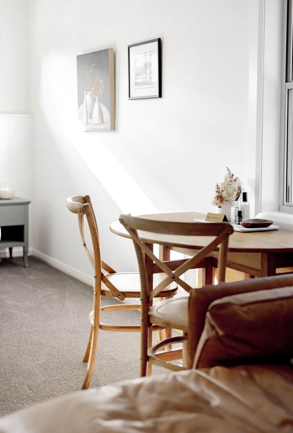 Una habitación acogedora con una mesa redonda de madera, dos sillas de madera, una mesita auxiliar y un ventanal con vistas.