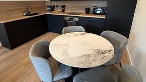 Una cucina moderna con pensili scuri, un tavolo rotondo in marmo e sedie rivestite in grigio.