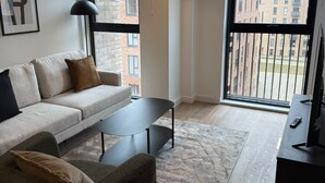 Un soggiorno moderno con un divano, un tavolino da caffè e un mobile TV. Sono presenti due ampie finestre con vista sugli edifici.
