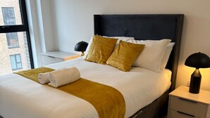 Un letto rifatto con cura, una toeletta con una lampada e vista su un edificio all'esterno.