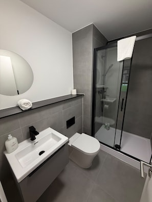 Et moderne badeværelse med en glasvæg omkring brusenichen, en hvid vask og et toilet.