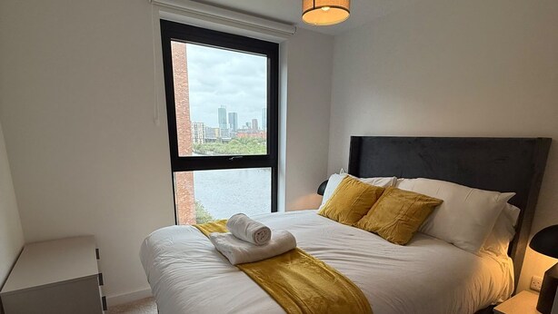 Ein Hotelzimmer mit einem Bett, einem Fenster mit Blick auf die Stadt, einem Nachttisch und einer Lampe.