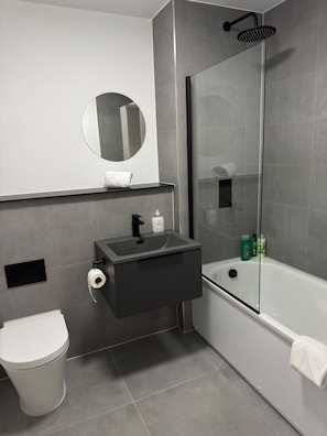 Une salle de bain moderne équipée de toilettes, d’un lavabo, d’un miroir et d’une douche.