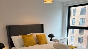 Ein ordentlich bezogenes Bett mit weißer und gelber Bettwäsche, ein dunkles Kopfteil und eine Nachttischlampe.
