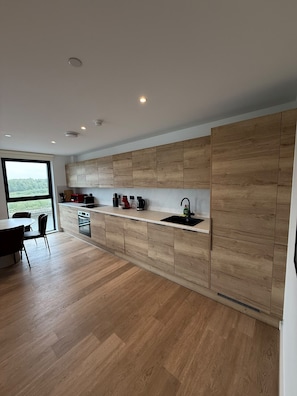 Une cuisine moderne avec des meubles de rangement en bois, un évier noir et un coin repas comprenant une table et des chaises.