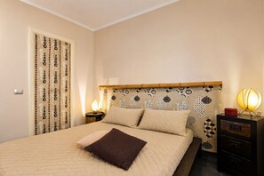 Ein ordentlich bezogenes Bett mit einer gesteppten Decke, einer Nachttischlampe und einem Nachttisch mit Lampe.