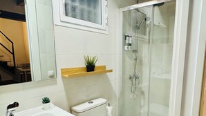 A bathroom with a white sink, wooden vanity, a toilet, a glass shower enclosure, and a small potted plant on a shelf. - "Your Charming Retreat" Apartment with a Mezzanine in Alegría de Jerez (Jerez de la Frontera)