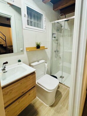 Een badkamer met een wit wastafelmeubel, een toilet, een douchecabine met glazen wanden, en een kleine potplant op een plankje.
