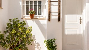 Ein weißes Gebäude mit einem Ziegeldach, einem Fenster mit einem Blumentopf, einer Tür und einer Wandleuchte.
