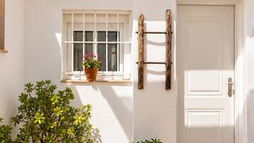 Un edificio blanco con techo de tejas, una ventana con planta en maceta, una puerta y una lámpara fijada a la pared.
