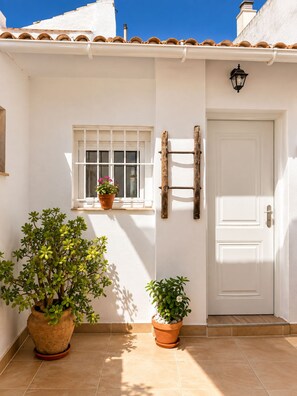 Un edificio bianco con tetto in tegole, una finestra con un vaso di fiori, una porta e un fiorile a parete.