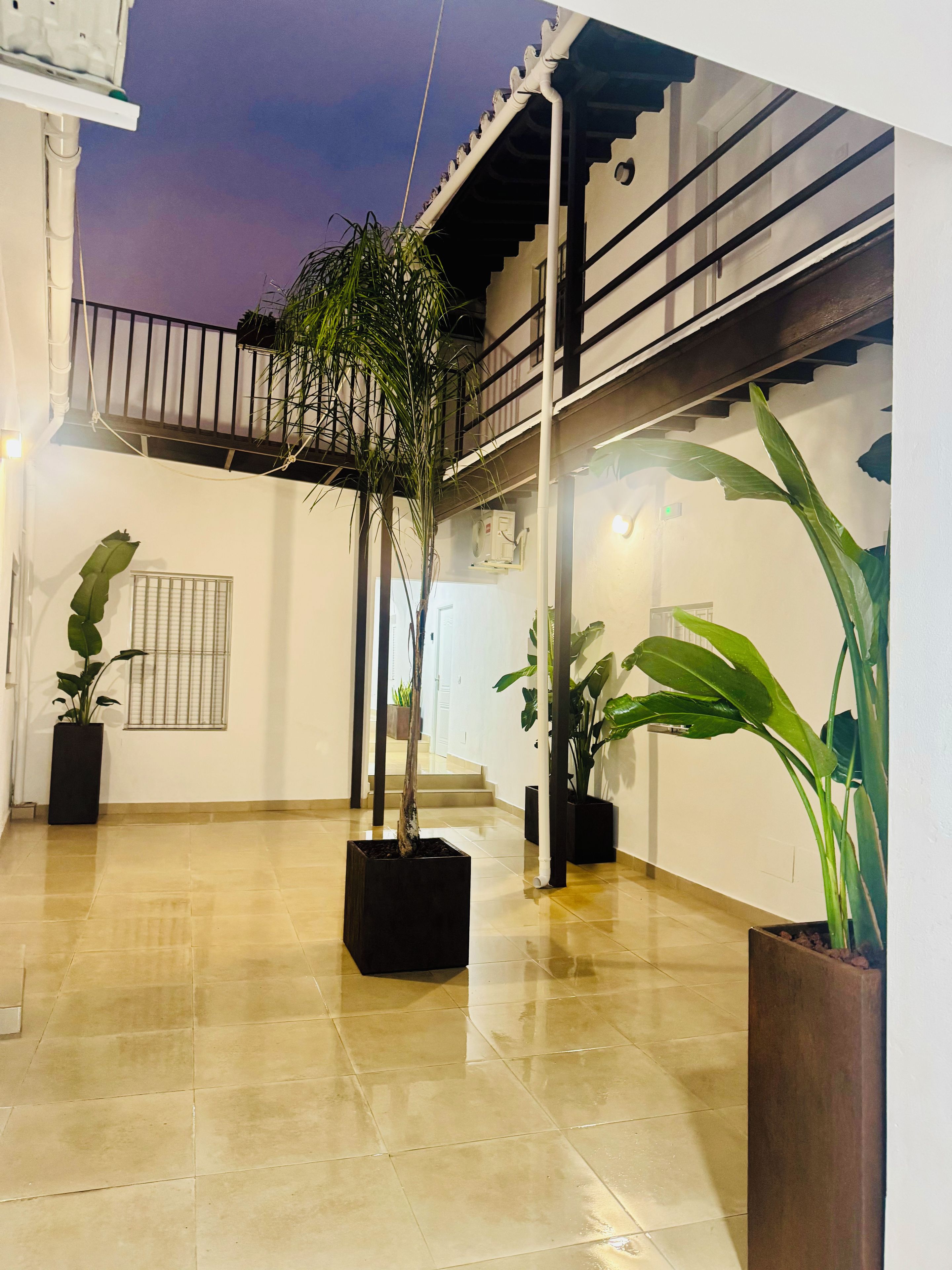 A spacious courtyard with tiled flooring, potted plants, a staircase, and a balcony with railings.