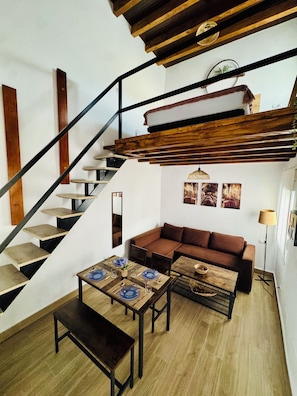 A modern interior with a staircase, a sofa, a coffee table, and a dining table set for four. - "Your Charming Retreat" Apartment with a Mezzanine in Alegría de Jerez (Jerez de la Frontera)