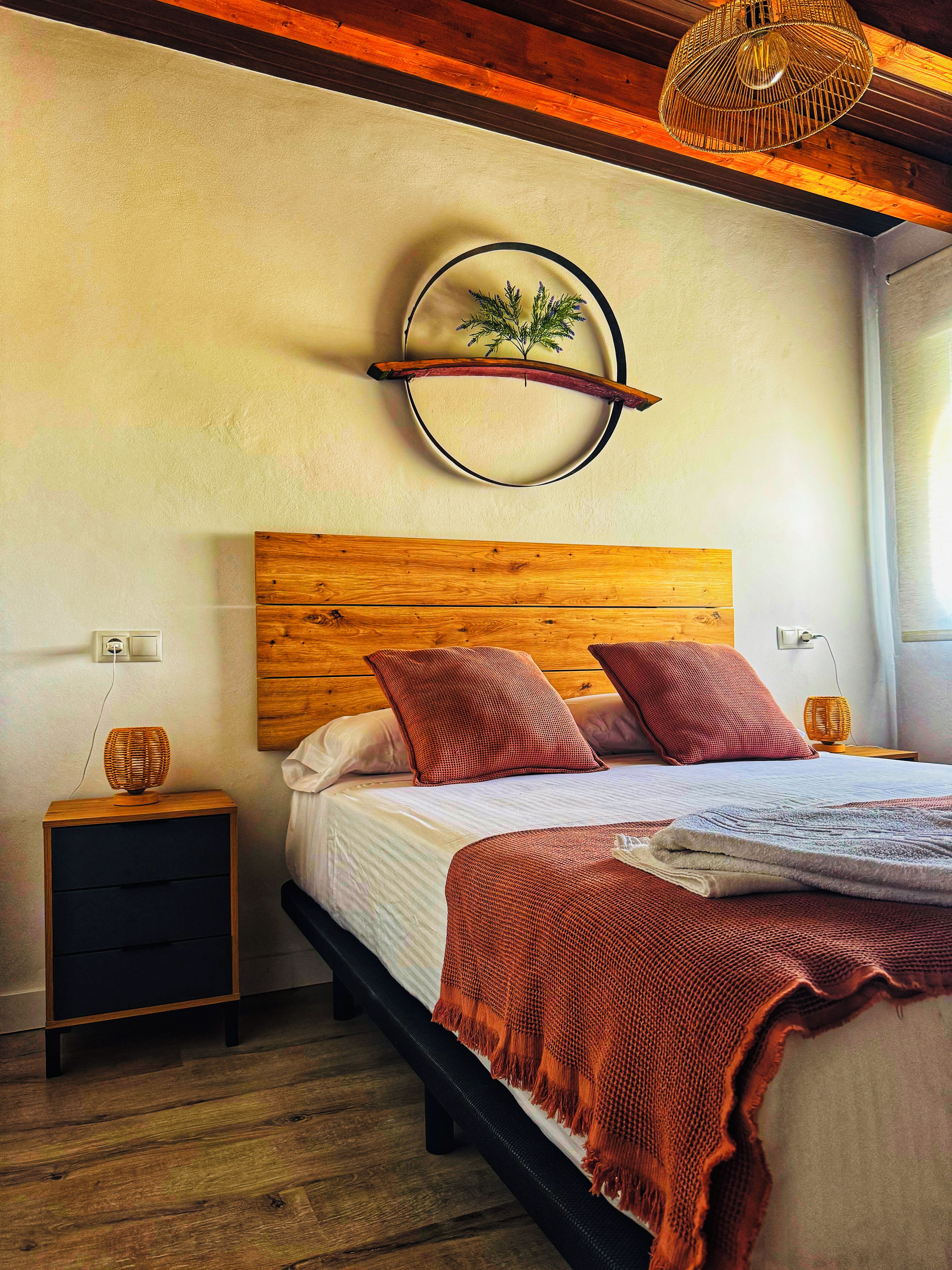 Una camera da letto con una testiera in legno, un letto con cuscini rossi, un comodino con una lampada e un decoro circolare a parete.