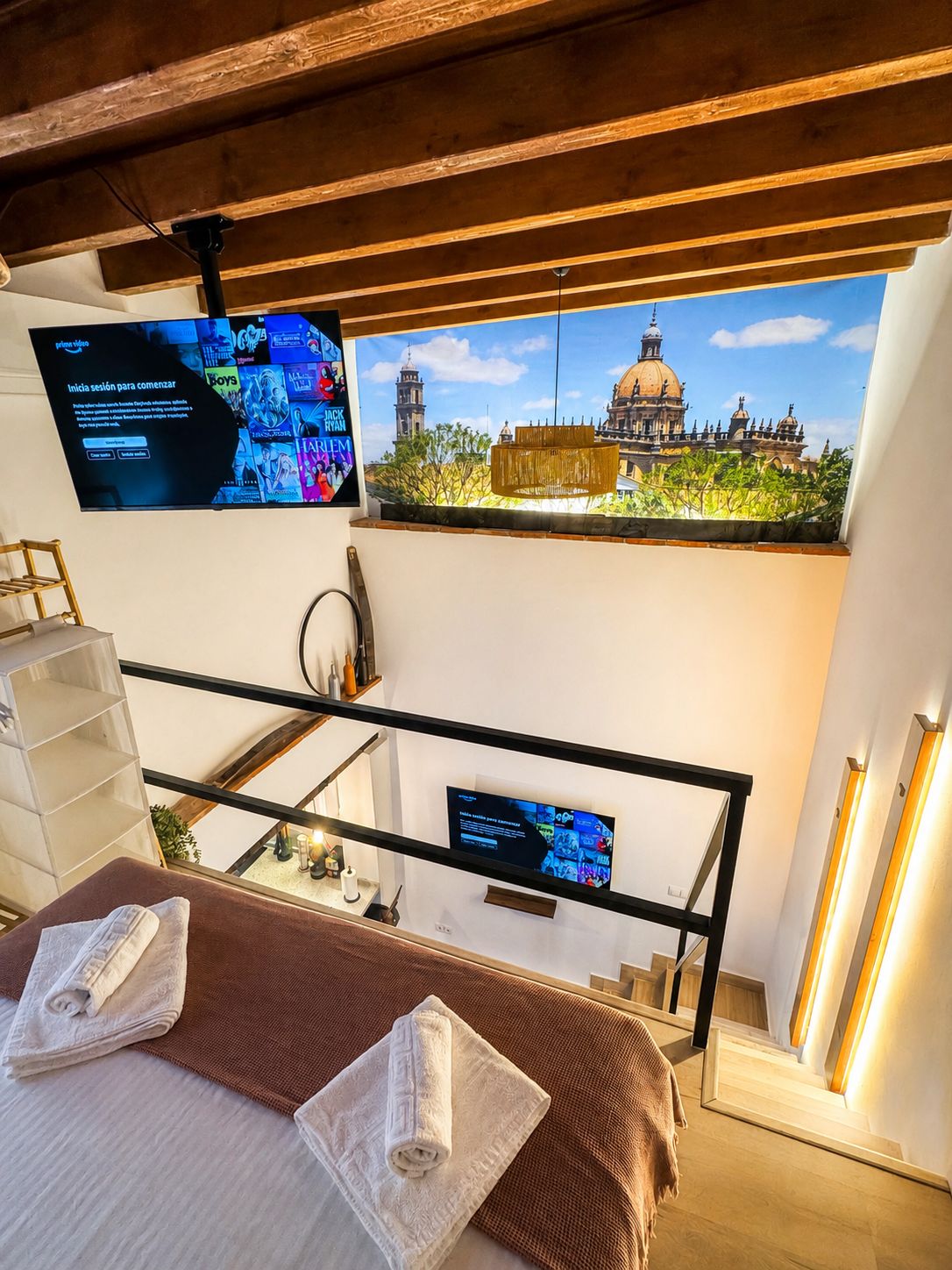 Habitación de hotel con una cama, un televisor montado en la pared, vista a un edificio histórico y una escalera.