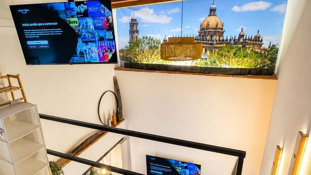 Ein Hotelzimmer mit Bett, einem an der Wand befestigten Fernseher, Blick auf ein historisches Gebäude und einer Treppe.