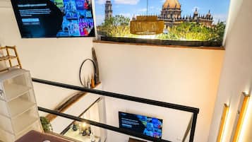 Habitación de hotel con una cama, un televisor montado en la pared, vista a un edificio histórico y una escalera.