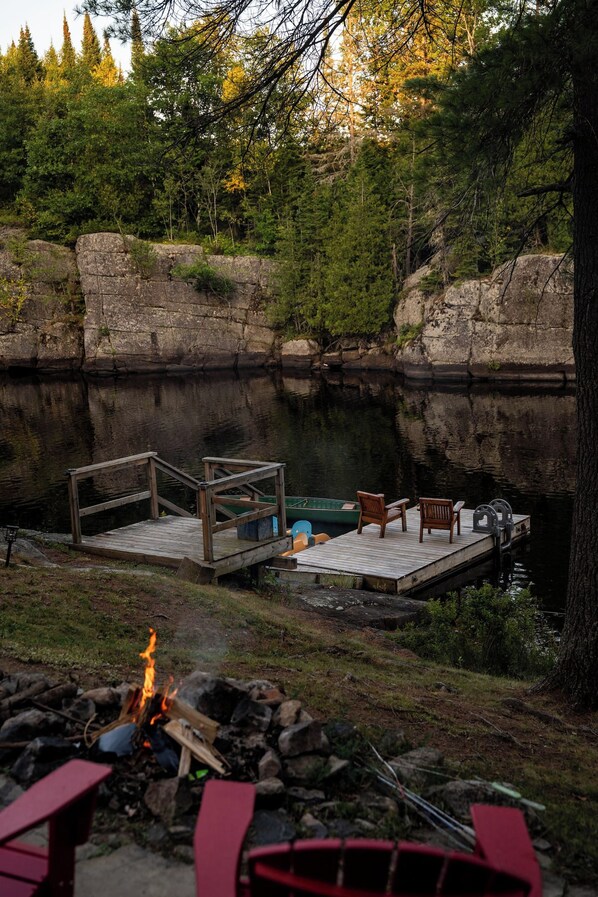 A lakeside dock with a fire pit, wooden deck, and chairs.