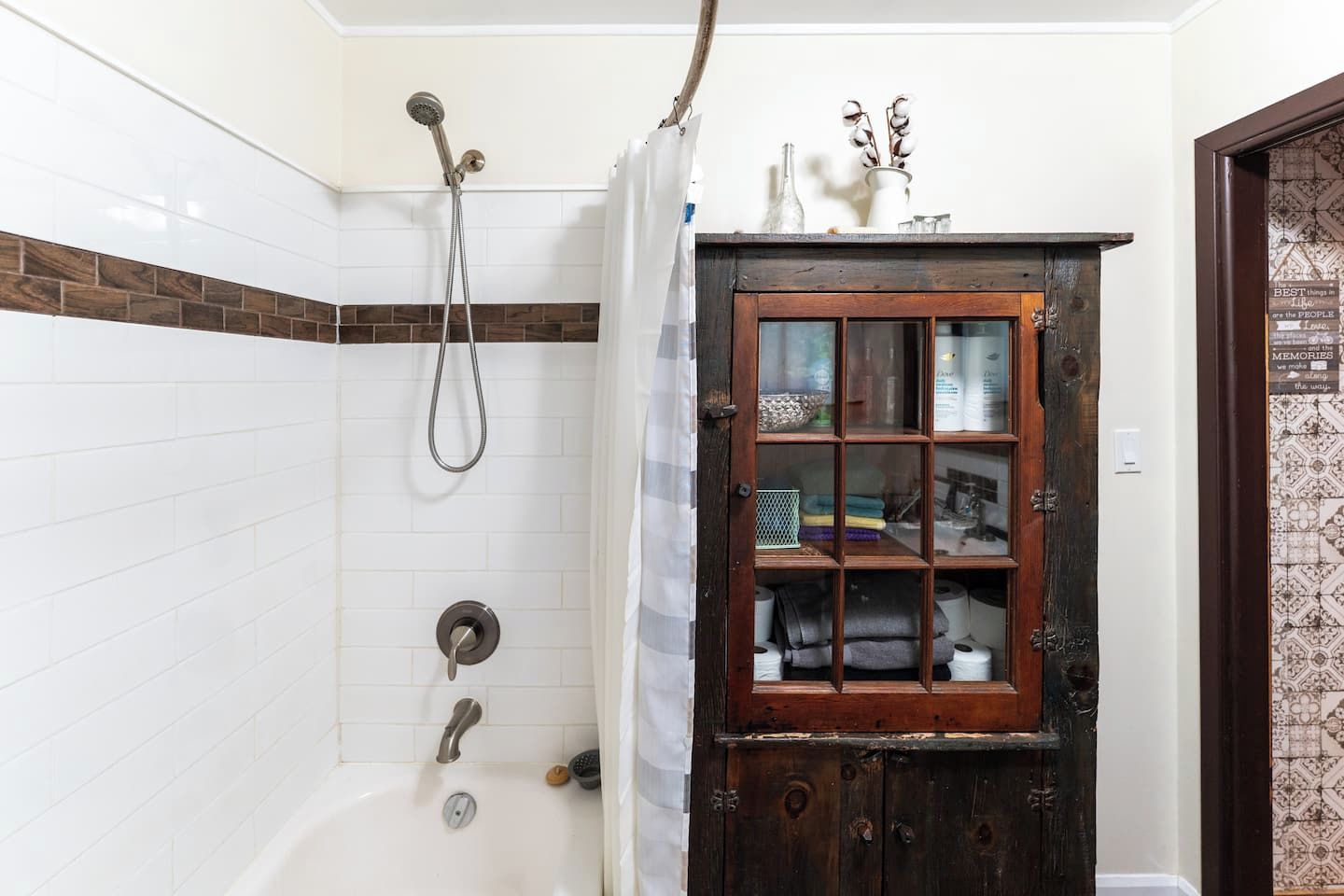 A bathroom with a shower, a wooden cabinet with glass doors, and a tiled wall.