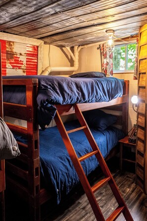 A bunk bed with a ladder, wooden walls, and a window with curtains.